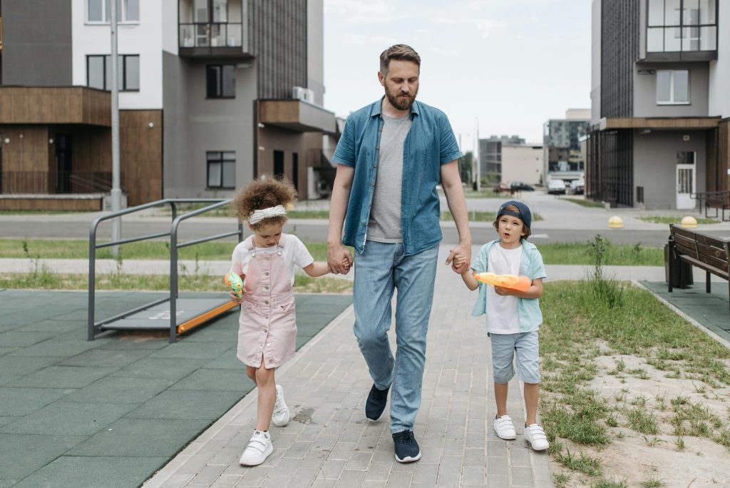 A father holding hands with his children outdoors on a sunny day, illustrating the importance of adjusting parenting plans for summer break with guidance from Family Lawyer Atlanta