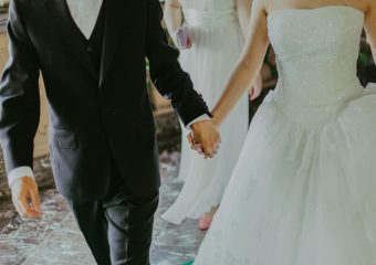 A romantic moment capturing a bride and groom holding hands in elegant wedding attire indoors.